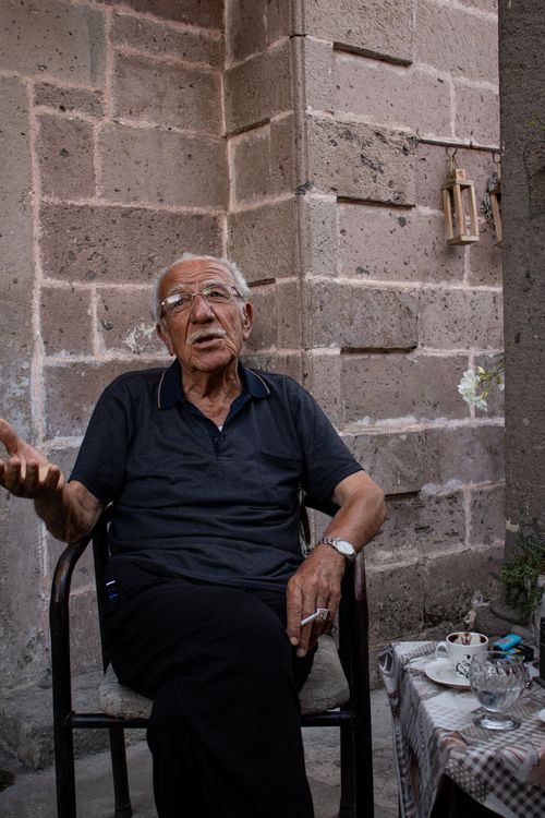 Free Senior man conversing while seated, holding a cigarette, beside a table with cups. Stock Photo