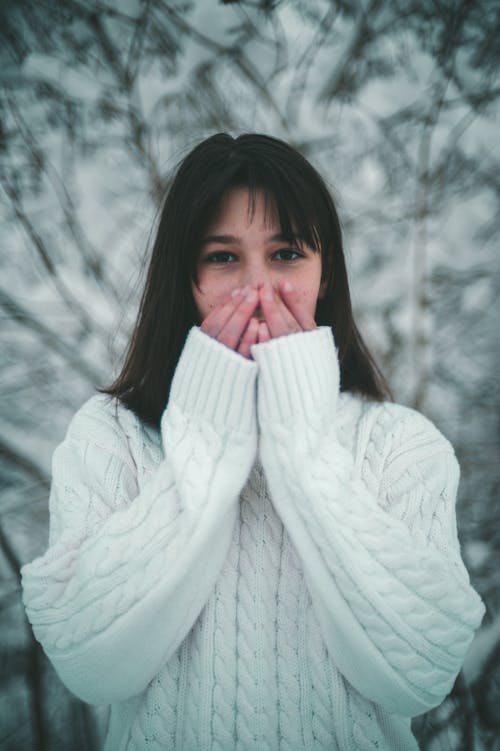 Photograph of a Woman in a White Sweater Covering Her Mouth