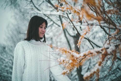 Free A woman in a white sweater stands by a snow-covered tree in winter. Outdoor fashion photography in Ukraine. Stock Photo