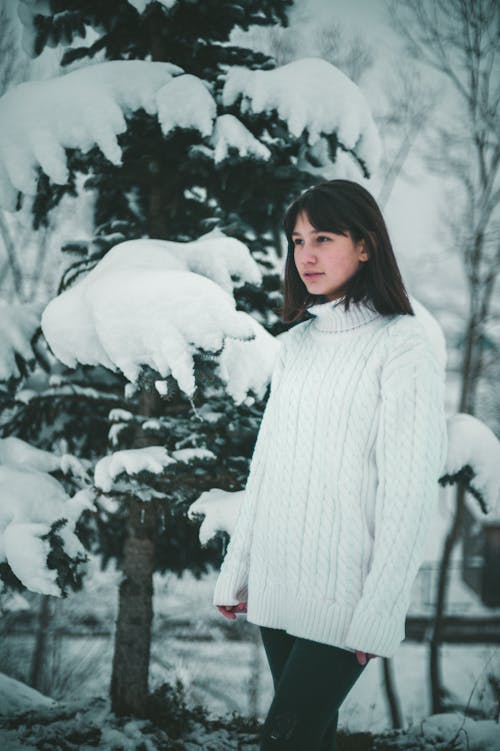 A Woman in White Knitted Sweater Standing Near the Snow Covered Tree