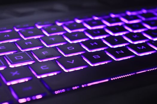 Close-up of a laptop keyboard glowing with vibrant purple neon lights, creating a futuristic tech vibe.