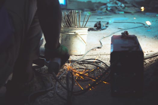 Close-up of a welder working indoors with visible sparks and tools.