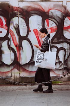 Stylish woman walking past graffiti in Milan carrying a gift bag.