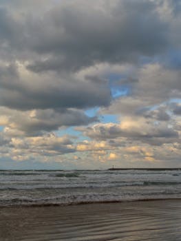 Scenic view of a stunning cloudy sky over a tranquil beach with gentle waves lapping the shore.