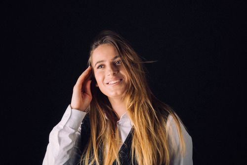 Free Studio portrait of a smiling woman with long hair and casual attire, set against a dark background. Stock Photo