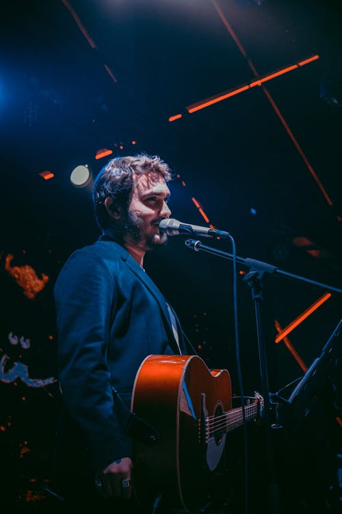 Man Holding a Guitar Standing in Front of a Microphone