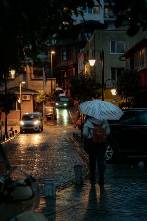 Free A person with a polka dot umbrella walks down a dimly lit cobblestone street after rain. Stock Photo