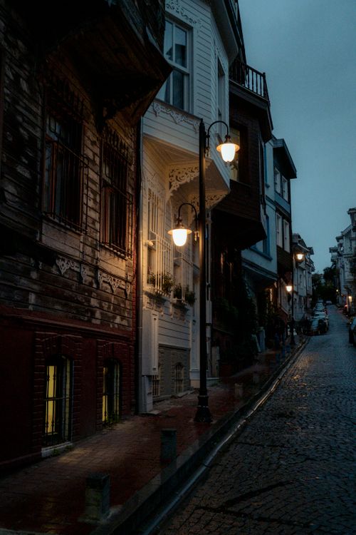 Free A moody evening street in an old town with lit street lamps and quaint architecture. Stock Photo