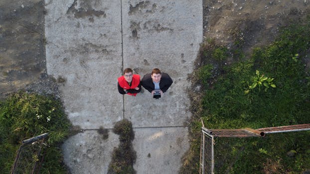Aerial shot capturing two men with a drone controller on a concrete pathway.