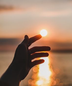 A silhouetted hand reaches towards the setting sun over the water in Eceabat, Turkey.