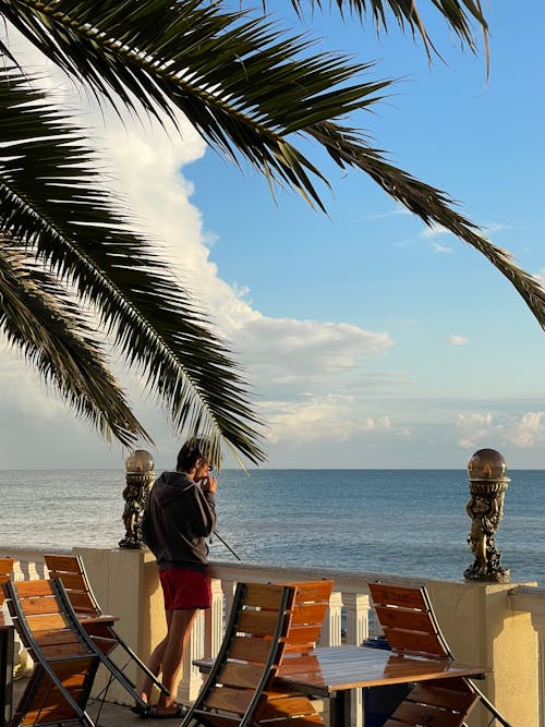 Photo of a Man Standing on a Terrace Overlooking the Ocean