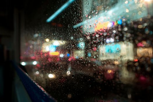 Close-up of raindrops on a window with blurred vibrant city lights.