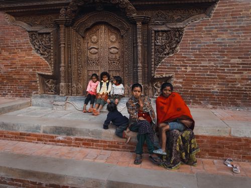 Free Family and children sit by an ornate wooden door on a brick structure, capturing local cultural elements. Stock Photo