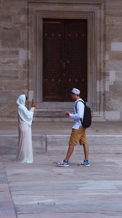 Photo of a Man and Woman Taking Pictures in Front of an Old Door