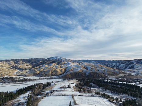 Aerial view of snow-covered hills and fields under a partly cloudy sky, highlighting a serene winter landscape.