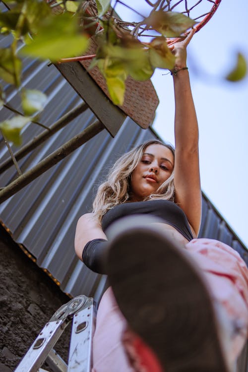 Woman in a Ladder Holding on the Basketball Ring