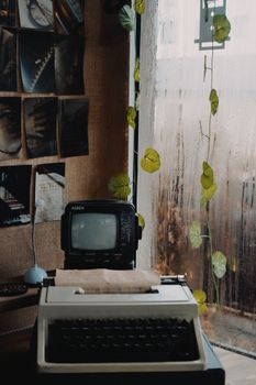 A retro setup featuring a typewriter and portable TV beside a rain-streaked window.