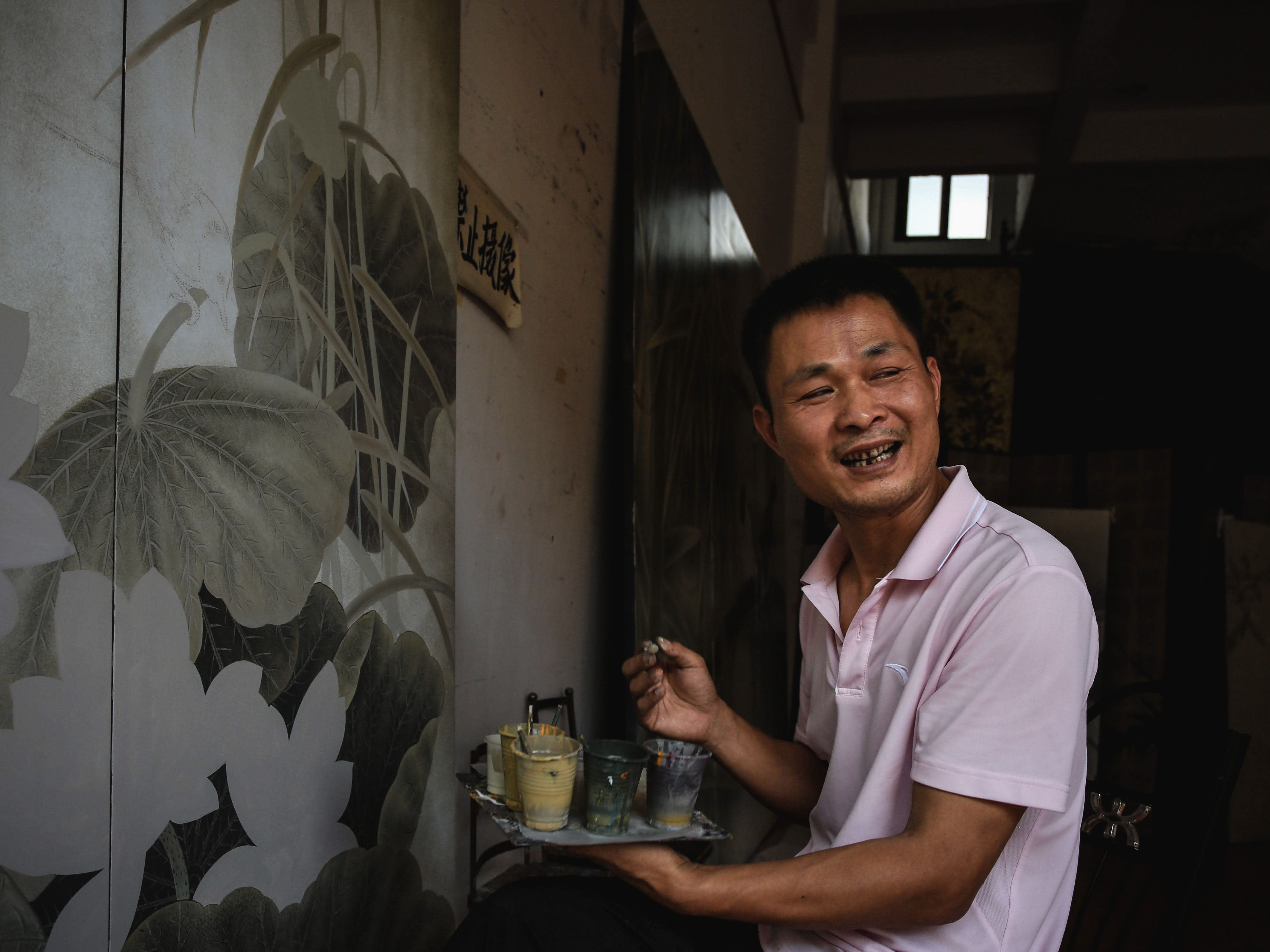 Artist smiling while painting mural indoors, using plastic cups for paints.