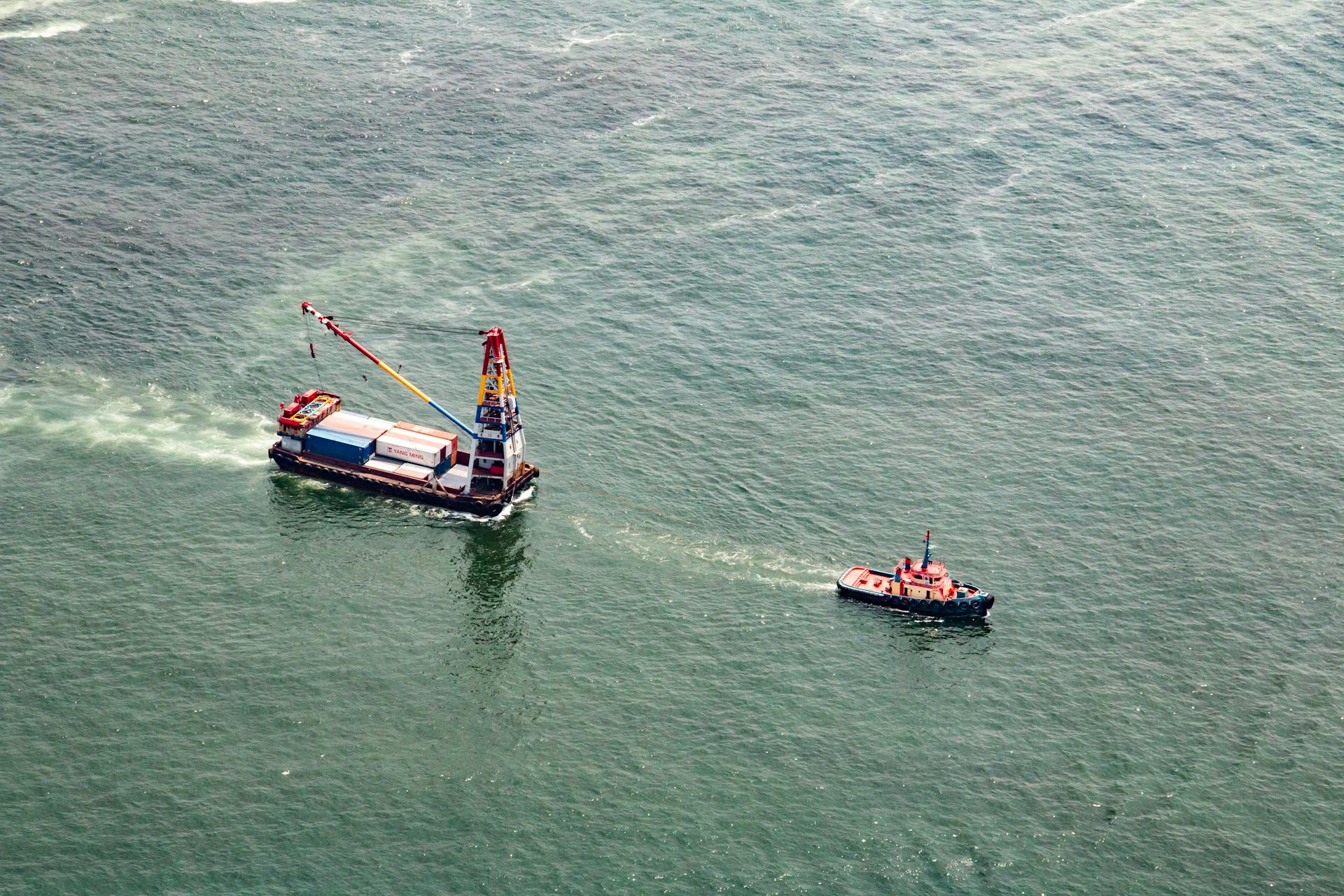 Aerial image of a tugboat and crane ship navigating the waters of Hong Kong harbor.