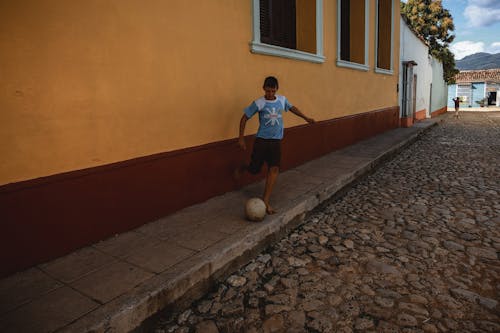 Boy Kicking a Soccer Ball on a Cobblestone Street