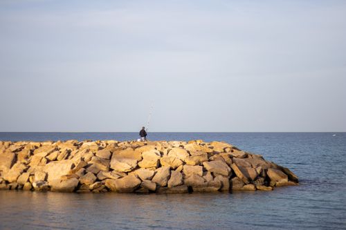 Free A lone fisherman enjoys a peaceful day at the rocky seaside in Mahdia, Tunisia. Stock Photo