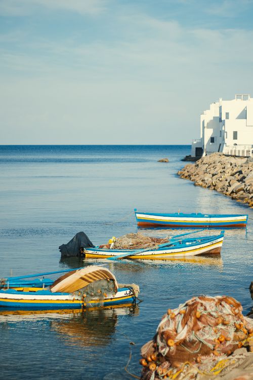 Free Traditional boats docked by the shore in Mahdia, Tunisia, with white buildings in the background. Stock Photo