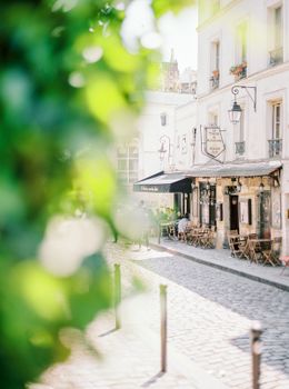 Sunlit cobblestone street with cozy café seating, surrounded by historic architecture.