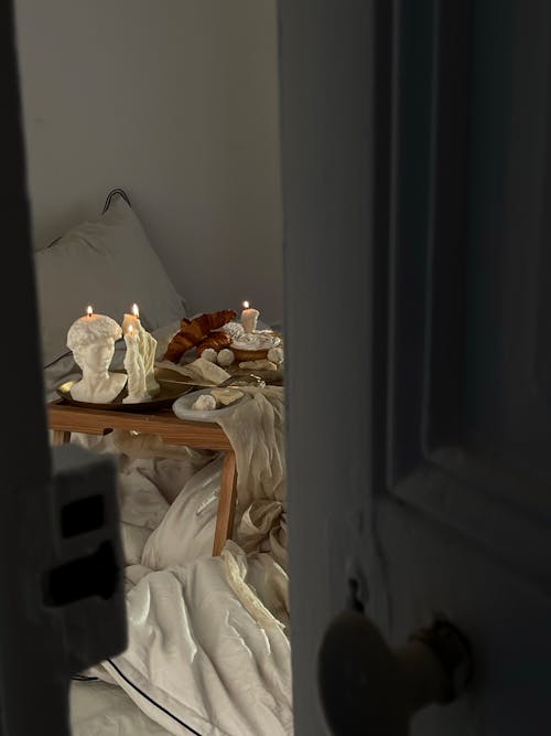Candles Burning on a Table Standing on a Bed Seen From Behind a Half-Opened Door