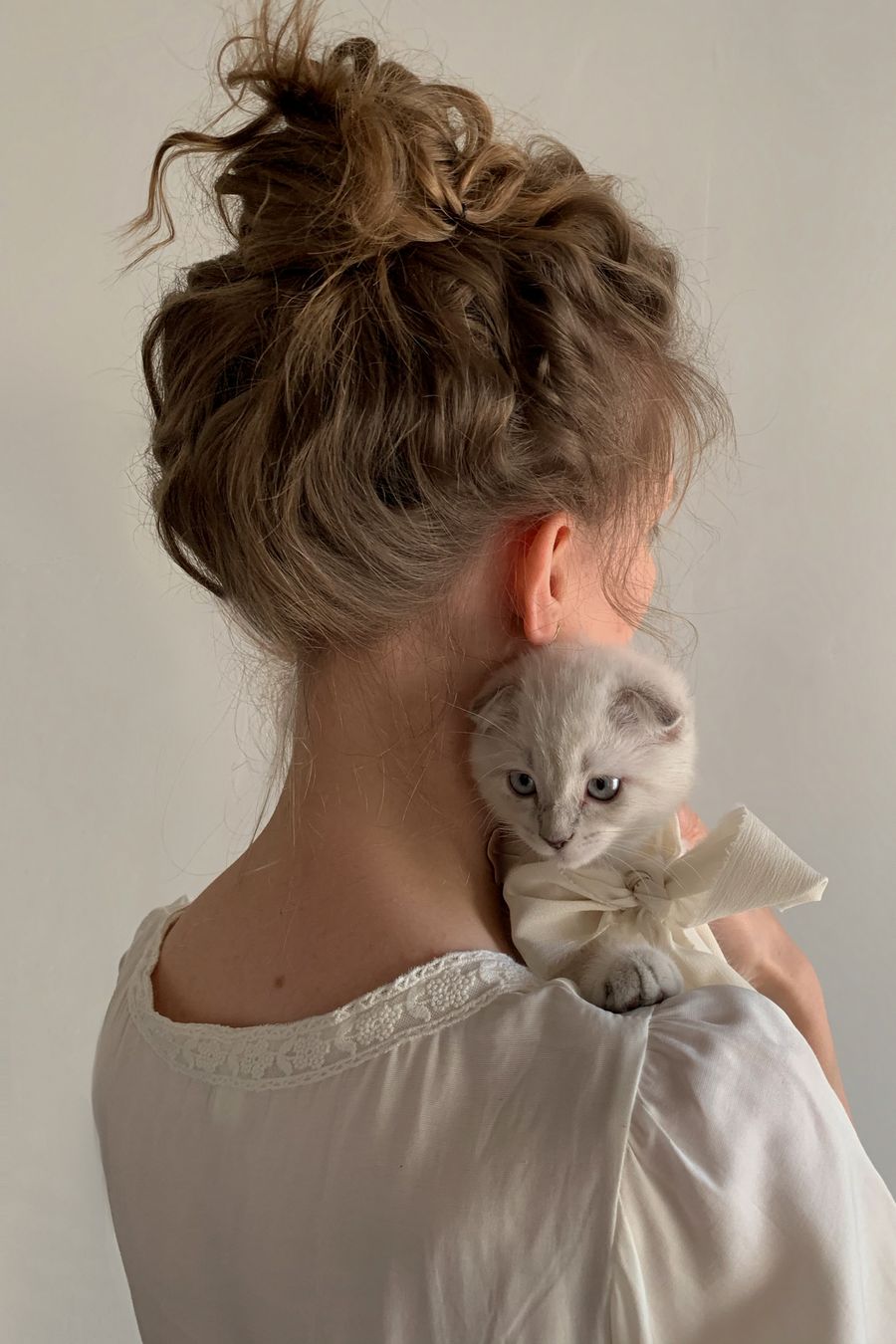 A young woman holding a kitten against a plain wall