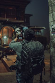 A photographer with equipment capturing night scenes outdoors with a backpack.