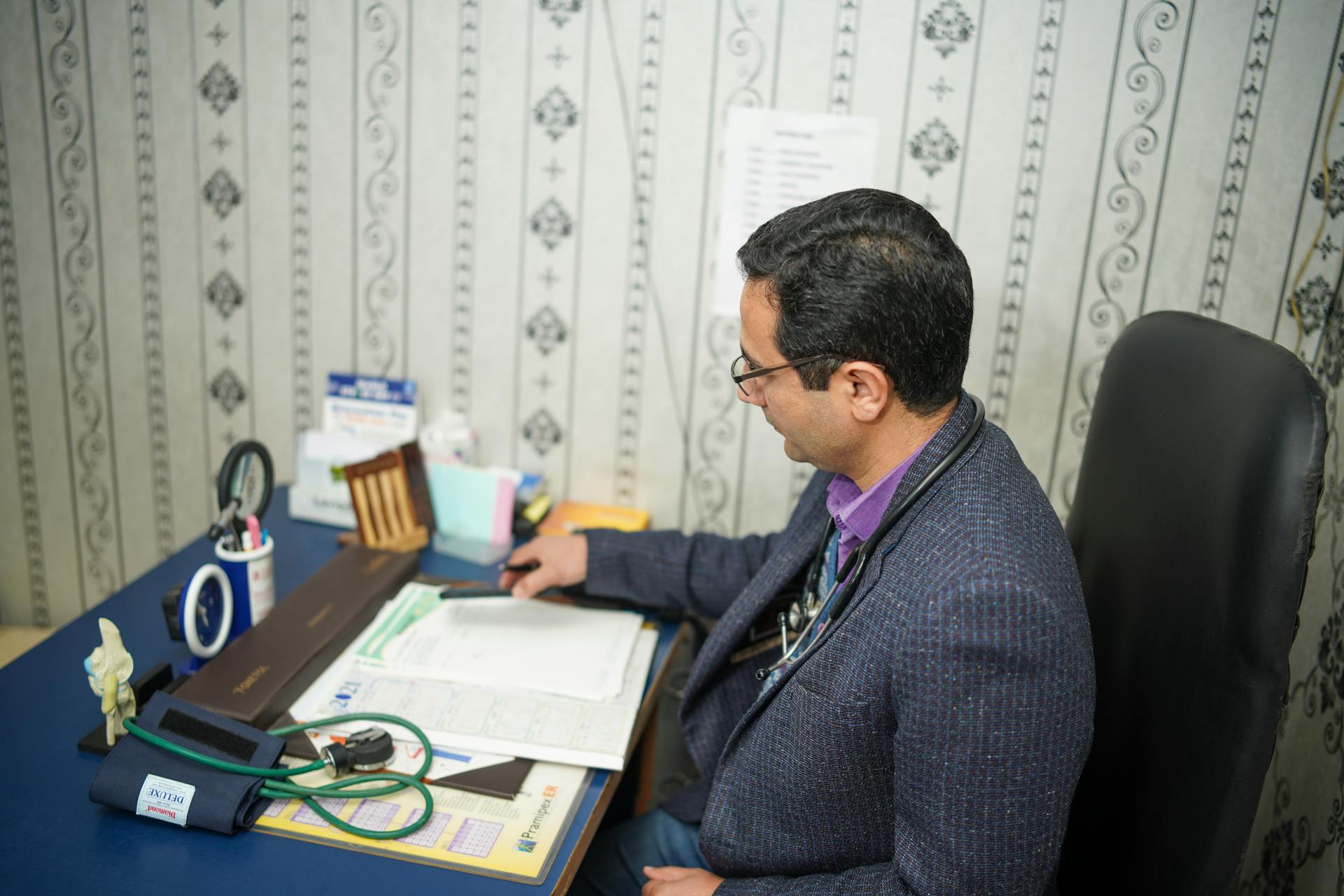 Doctor reviewing medical documents at desk in clinic office.