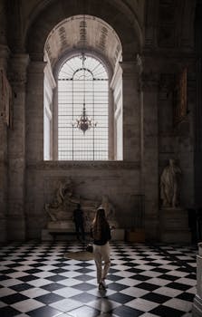 A person walks inside a historic cathedral with a magnificent checkered floor and arched window.