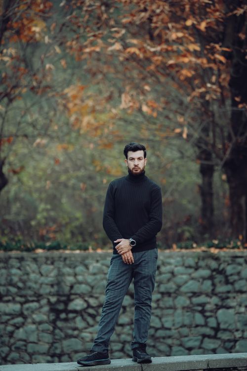 Free A young man in a black turtleneck poses elegantly with fall foliage in the background. Stock Photo
