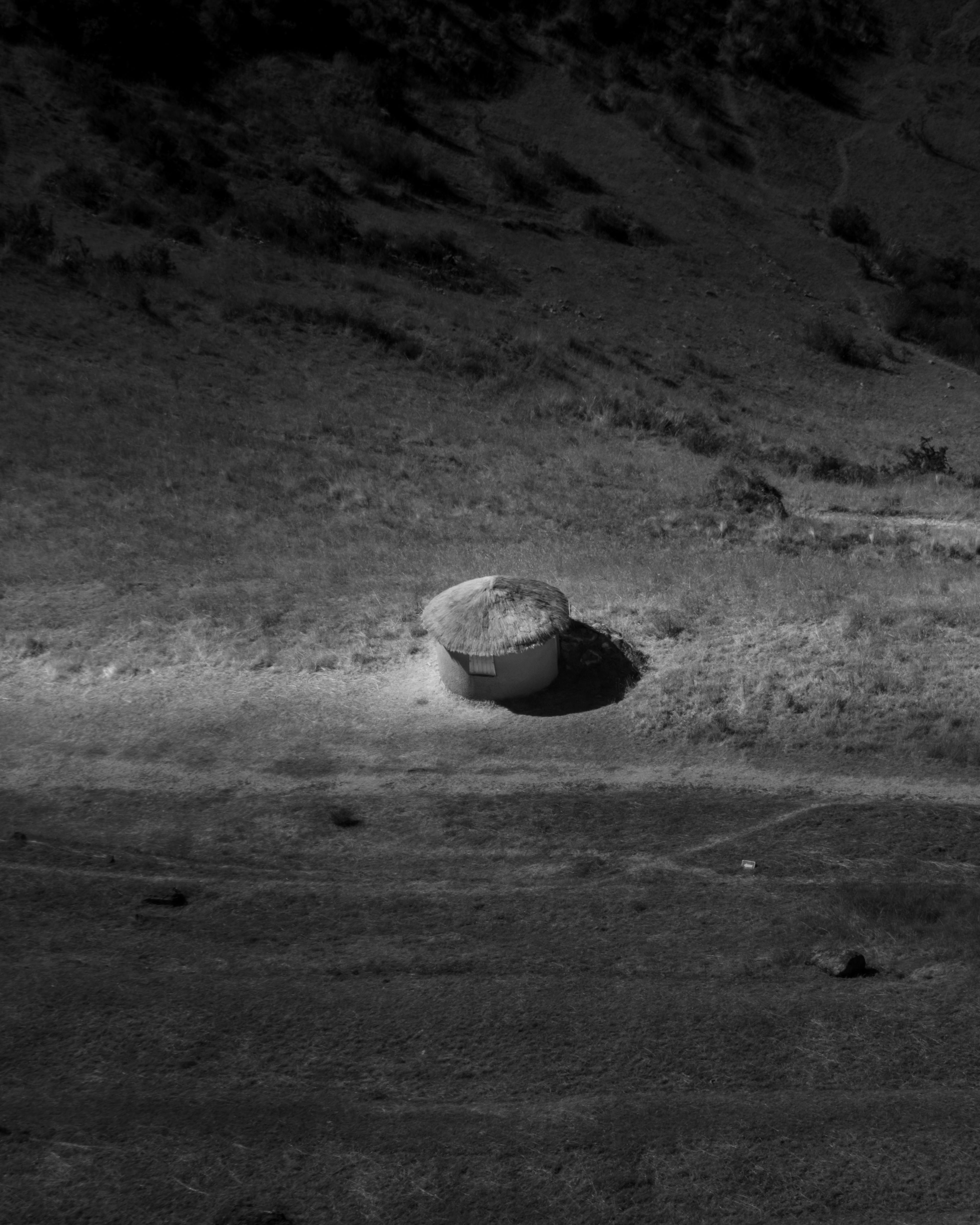 Black and white aerial shot of a solitary hut in the vast Peruvian desert landscape.