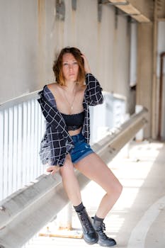 Stylish young woman poses on urban bridge, embodying modern city fashion.