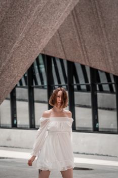 Stylish woman posing in white dress against contemporary architectural backdrop.