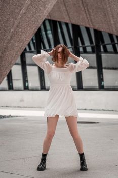Woman posing confidently in a white dress against a modern architectural background.