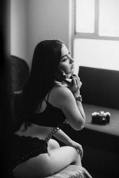 Black and white image of woman in lingerie using vintage telephone by a window.