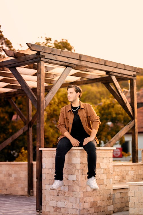 Man in Brown Long Sleeves Sitting on a Wall