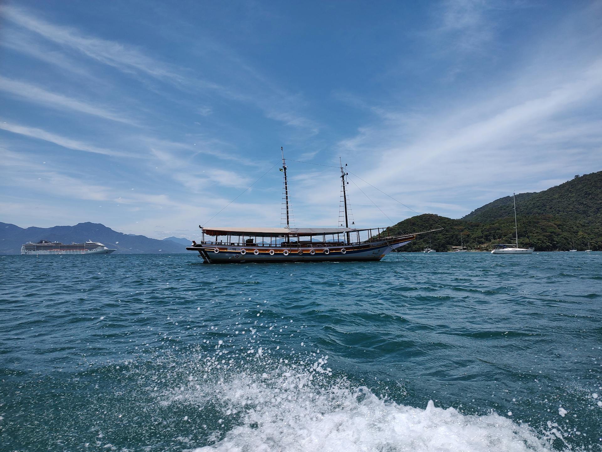 A classic schooner sails under blue skies near RJ, Brazil, offering a scenic view of the ocean.