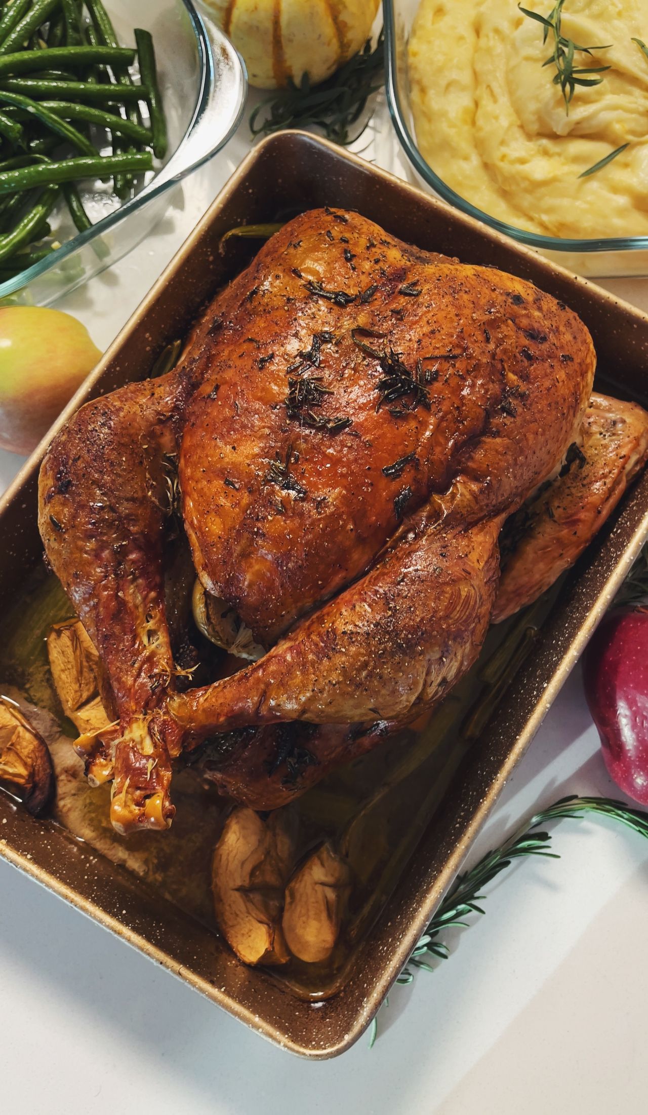 Golden roasted turkey in a roasting pan surrounded by green beans and mashed potatoes