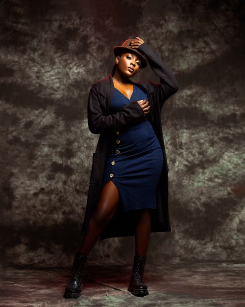 Free Fashionable woman in blue dress and black coat posing confidently with a hat. Stock Photo