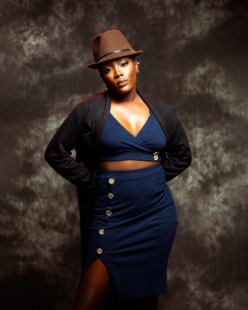 Free Confident woman in fashionable blue dress and brown hat against a textured backdrop. Stock Photo