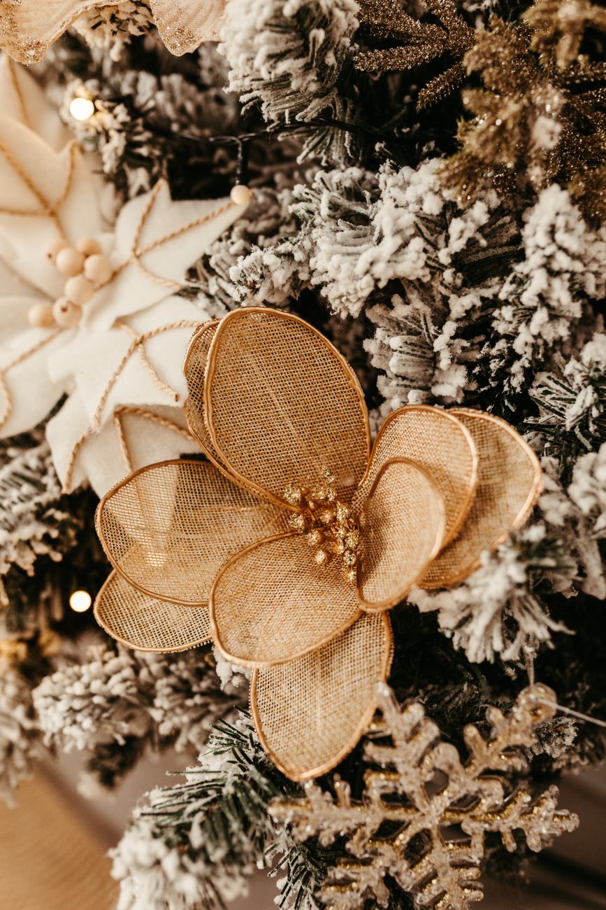 Close-up de decorações florais douradas e brancas em uma árvore de Natal com galhos cobertos de neve.