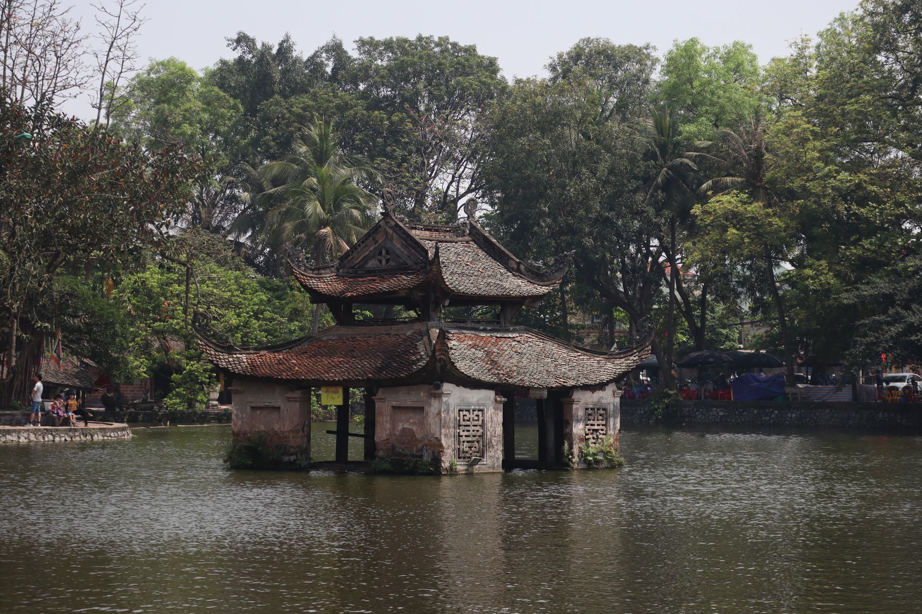 Historic temple with traditional architecture by a calm river surrounded by lush summer foliage.