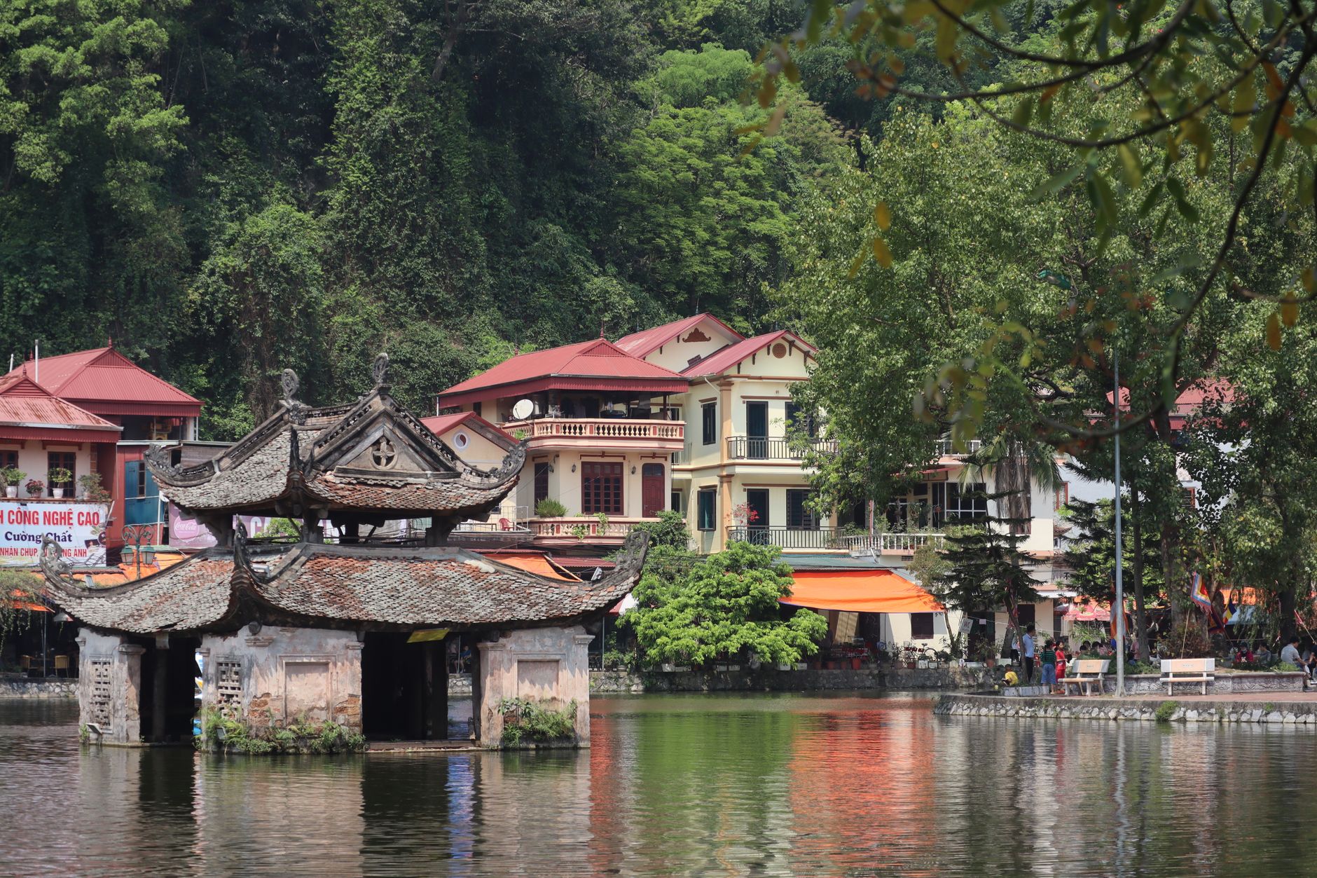 A tranquil landscape featuring a historic temple on a river, surrounded by lush greenery and vibrant buildings.