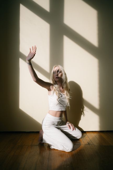 Artistic portrait of a woman kneeling indoors in sunlight with window shadow patterns.