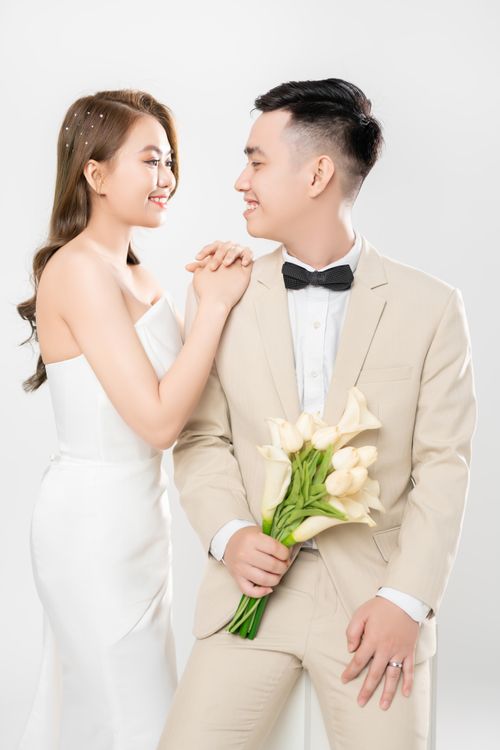 Free Smiling Asian bride and groom in stylish wedding outfits holding a bouquet. Stock Photo