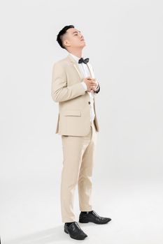 Asian groom in a beige suit posing with eyes closed and hands clasped.
