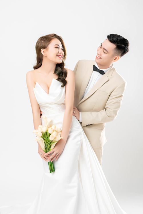 Free Smiling couple posing elegantly in wedding attire with a bouquet in a bright studio setting. Stock Photo